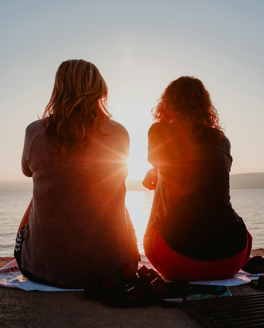 Two friends sitting together at sunset, facing the water